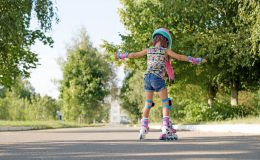 Kid tries to keep his balance and not fall, for the first time standing on roller skates. view behind. A girl is learning to rollerblade. Active sports for summer recreation and outdoor entertainment